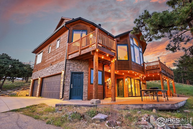 view of front facade featuring a deck, a garage, stone siding, and driveway