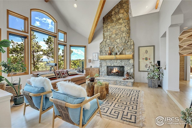 living area with a stone fireplace, wood finished floors, baseboards, and high vaulted ceiling