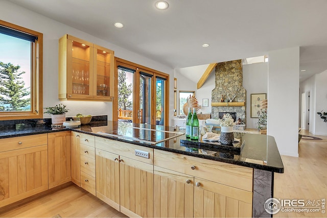 kitchen featuring light brown cabinets, open floor plan, dark stone countertops, a peninsula, and black electric cooktop