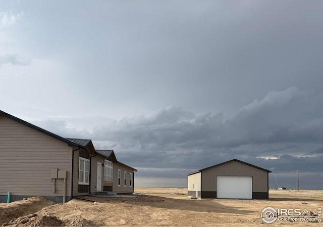 view of home's exterior featuring a standing seam roof, a garage, an outbuilding, metal roof, and driveway