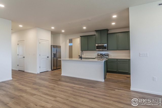 kitchen featuring light hardwood / wood-style floors, green cabinets, sink, an island with sink, and stainless steel appliances