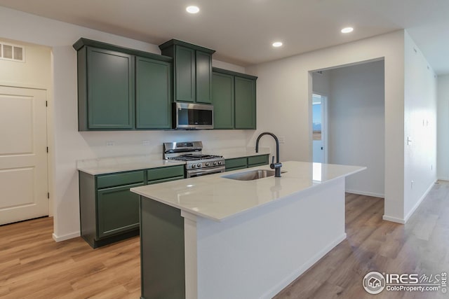 kitchen with sink, a kitchen island with sink, light stone countertops, appliances with stainless steel finishes, and green cabinetry