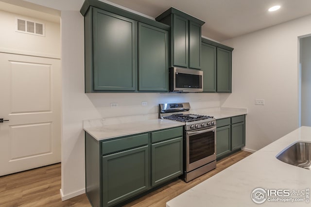 kitchen with light wood-type flooring, light stone countertops, appliances with stainless steel finishes, and green cabinetry