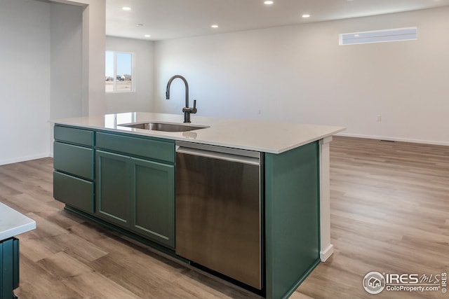 kitchen featuring sink, a kitchen island with sink, green cabinetry, stainless steel dishwasher, and light hardwood / wood-style flooring