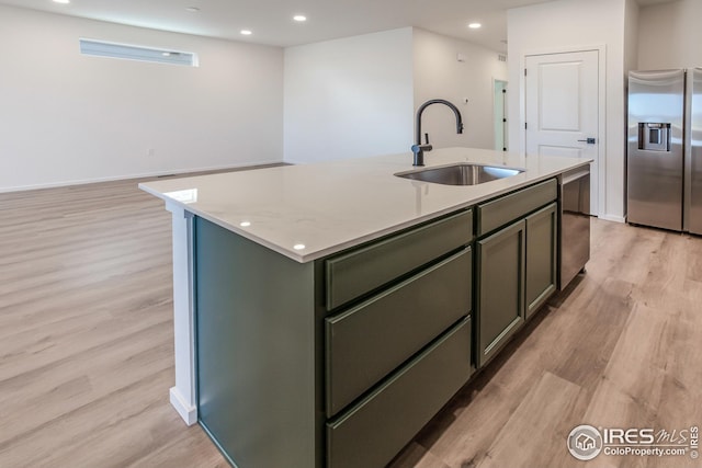 kitchen with appliances with stainless steel finishes, an island with sink, sink, light stone counters, and light hardwood / wood-style flooring