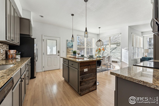 kitchen featuring hanging light fixtures, backsplash, light wood-style flooring, light stone countertops, and dishwasher