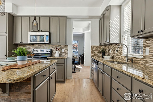 kitchen with stainless steel appliances, a sink, backsplash, and gray cabinetry