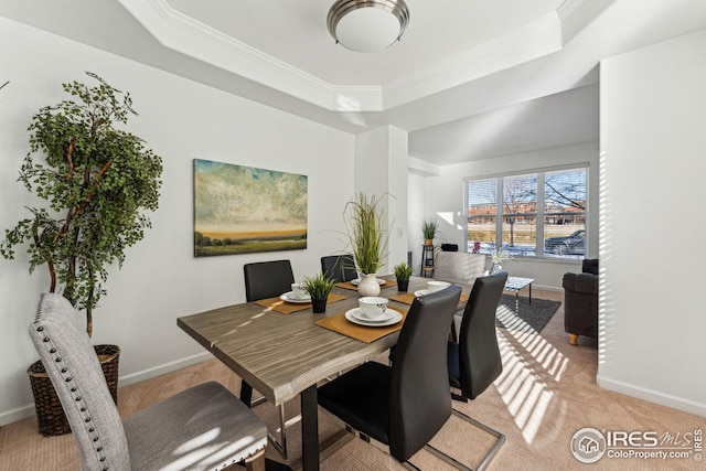 dining room featuring light carpet, baseboards, ornamental molding, and a raised ceiling