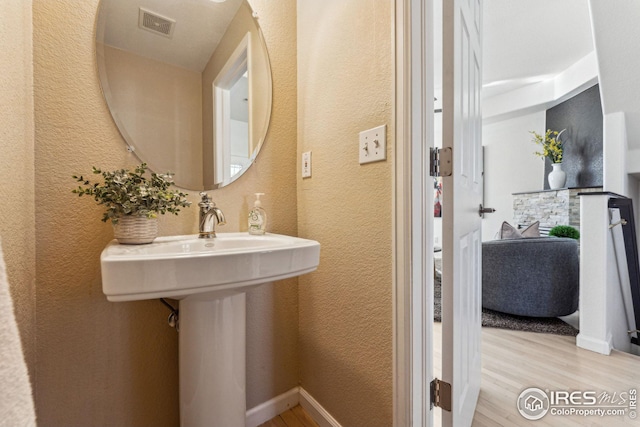 bathroom with visible vents, a textured wall, a sink, wood finished floors, and baseboards