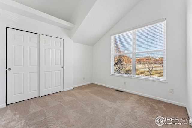 unfurnished bedroom with carpet, a closet, visible vents, vaulted ceiling, and baseboards