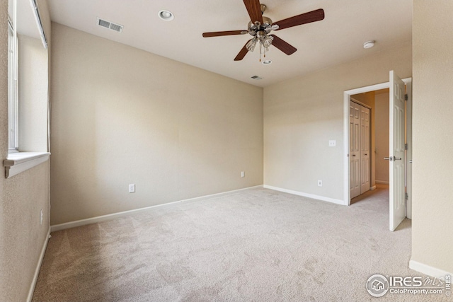 spare room featuring a ceiling fan, visible vents, light carpet, and baseboards