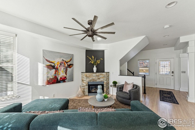 living area with light wood-style floors, a fireplace, baseboards, and a ceiling fan