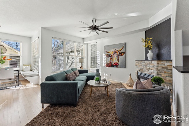 living room featuring hardwood / wood-style flooring, baseboards, a ceiling fan, and a stone fireplace