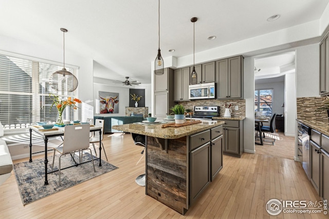 kitchen featuring light wood-style floors, stainless steel appliances, gray cabinetry, stone counters, and backsplash