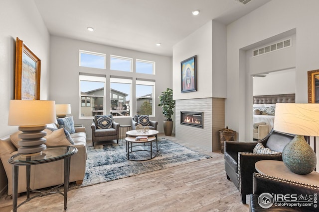 living area with visible vents, recessed lighting, wood finished floors, and a glass covered fireplace