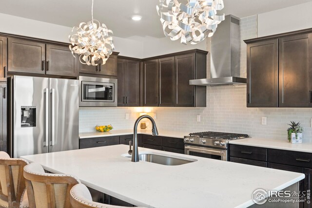 kitchen with sink, wall chimney range hood, tasteful backsplash, decorative light fixtures, and appliances with stainless steel finishes