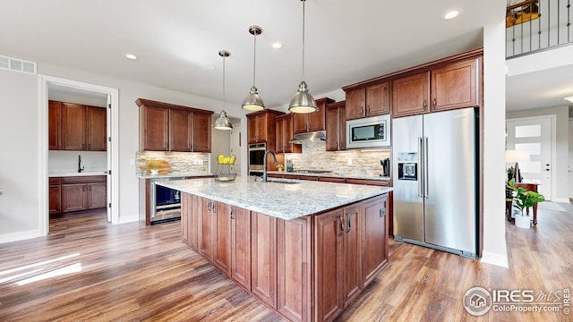 kitchen with under cabinet range hood, stainless steel appliances, a sink, visible vents, and light wood-type flooring