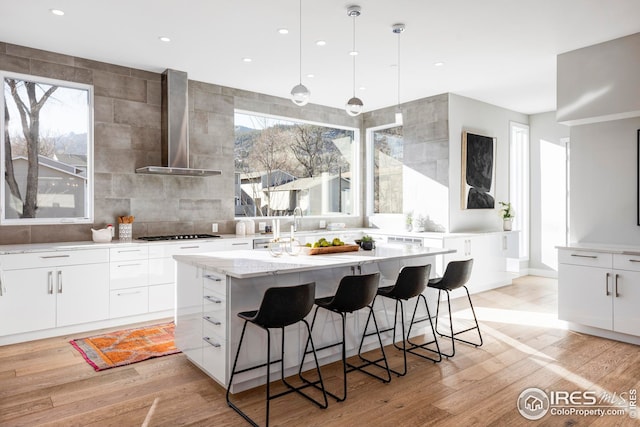 kitchen featuring an island with sink, black gas cooktop, tasteful backsplash, wall chimney range hood, and white cabinets