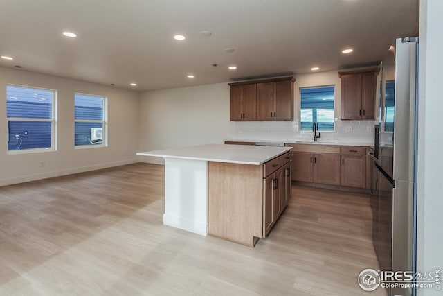 kitchen featuring light wood-type flooring, a center island, stainless steel fridge, sink, and backsplash