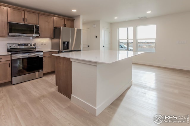 kitchen with light hardwood / wood-style floors, stainless steel appliances, tasteful backsplash, and a kitchen island