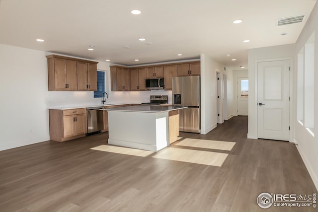 kitchen featuring sink, stainless steel appliances, wood-type flooring, and a center island