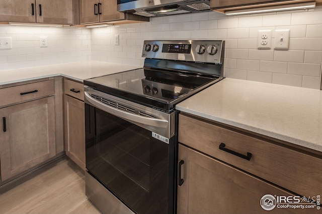 kitchen featuring light wood-type flooring, exhaust hood, electric stove, and backsplash