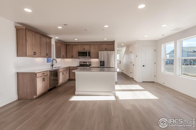 kitchen with light hardwood / wood-style floors, tasteful backsplash, a kitchen island, appliances with stainless steel finishes, and sink