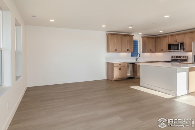 kitchen with a kitchen island, appliances with stainless steel finishes, light hardwood / wood-style flooring, and sink