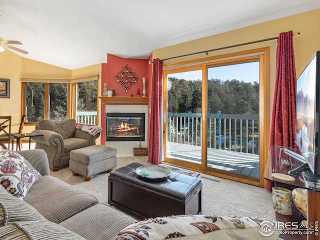 living room with a glass covered fireplace, vaulted ceiling, carpet, and a ceiling fan