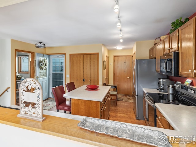 kitchen featuring brown cabinets, stainless steel range with electric stovetop, a kitchen island, black microwave, and light countertops