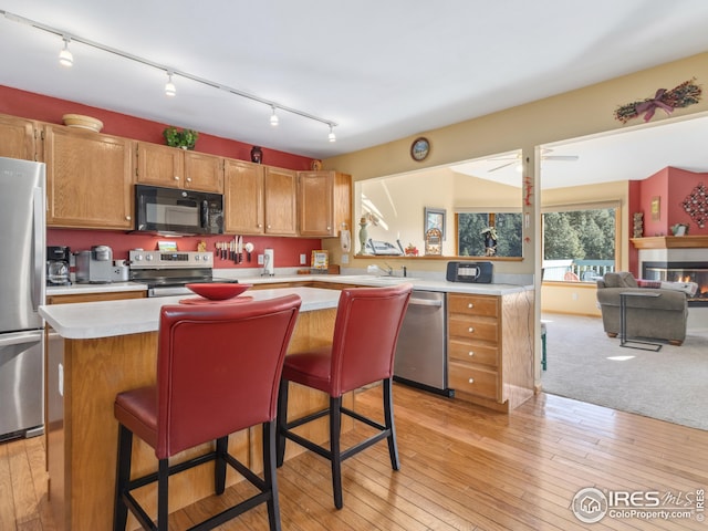 kitchen featuring light countertops, light wood-style floors, appliances with stainless steel finishes, a glass covered fireplace, and a center island