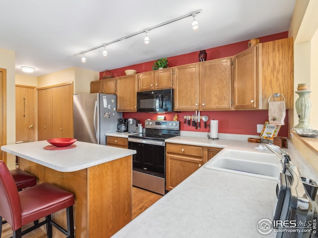 kitchen featuring a sink, stainless steel appliances, light countertops, a kitchen bar, and a center island