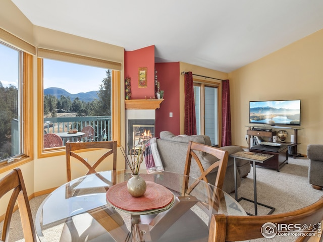 carpeted dining area with a glass covered fireplace, a mountain view, baseboards, and vaulted ceiling