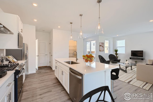 kitchen with appliances with stainless steel finishes, an island with sink, pendant lighting, white cabinets, and sink