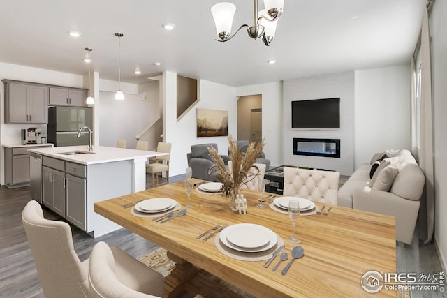 dining area with dark wood-type flooring, a large fireplace, sink, and a notable chandelier