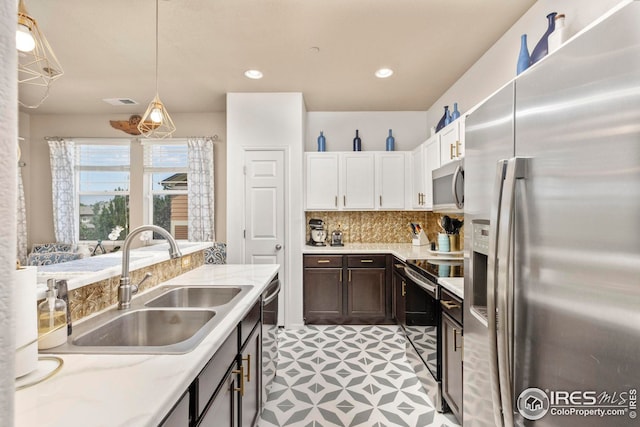 kitchen featuring decorative backsplash, appliances with stainless steel finishes, hanging light fixtures, white cabinetry, and a sink