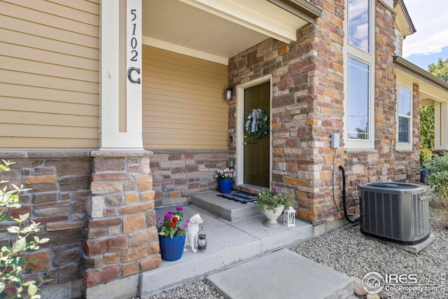 view of exterior entry featuring central AC and brick siding