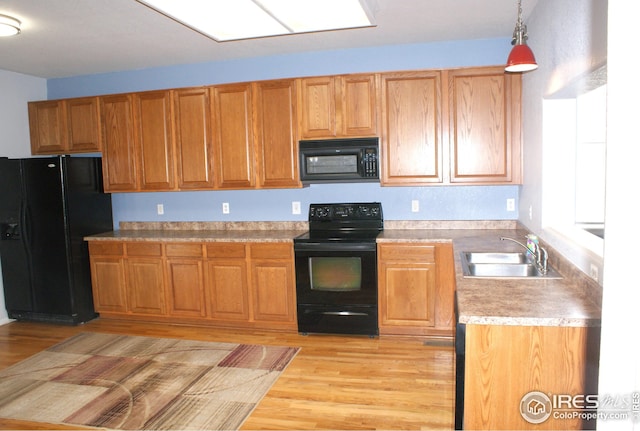 kitchen with light wood-type flooring, decorative light fixtures, sink, and black appliances