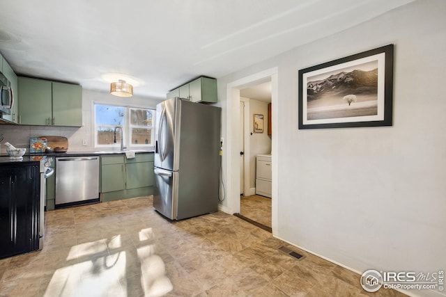 kitchen with tasteful backsplash, green cabinets, stainless steel appliances, and washer / clothes dryer