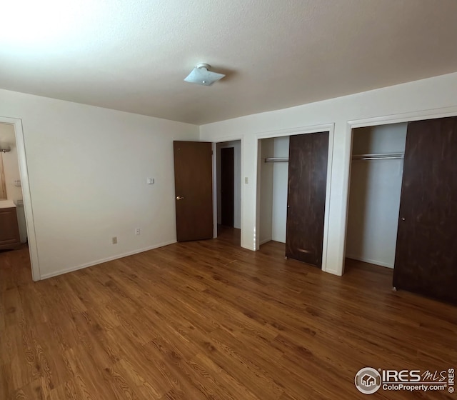 unfurnished bedroom with ensuite bathroom, dark hardwood / wood-style flooring, and multiple closets