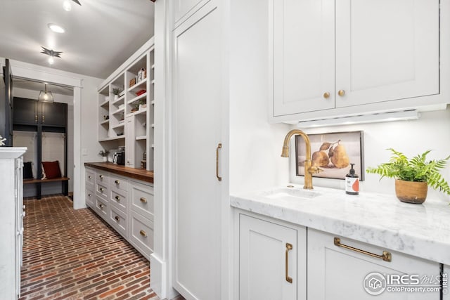 interior space featuring brick floor, white cabinetry, a sink, and open shelves