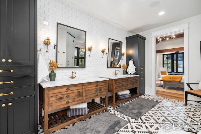 full bath featuring two vanities, decorative backsplash, a sink, and ensuite bathroom