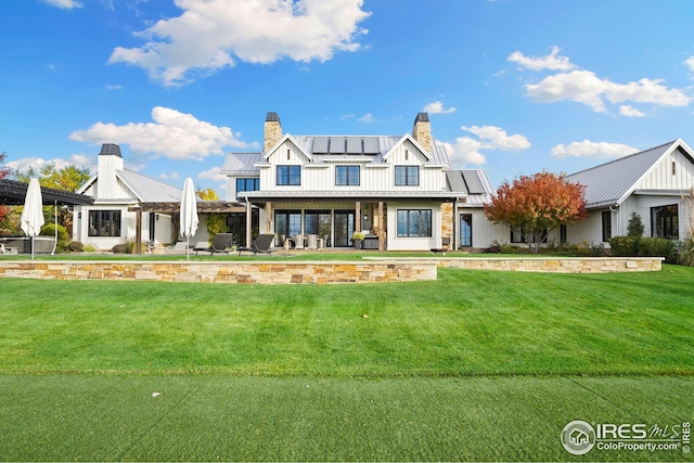 view of front of house with a front lawn, a standing seam roof, a chimney, and roof mounted solar panels