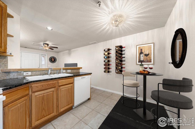 kitchen featuring light tile patterned flooring, dishwasher, dark stone counters, ceiling fan with notable chandelier, and sink