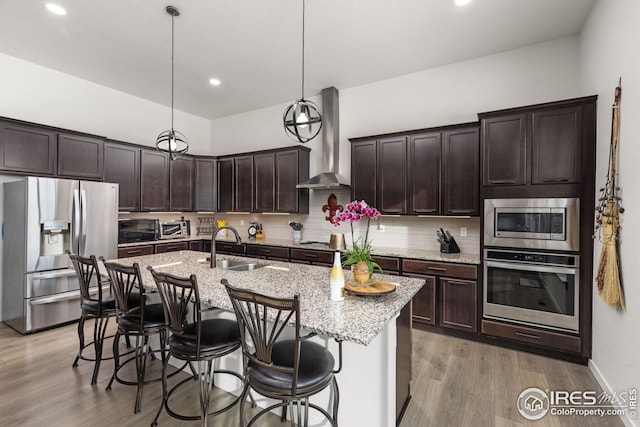 kitchen featuring pendant lighting, a kitchen island with sink, stainless steel appliances, and wall chimney exhaust hood