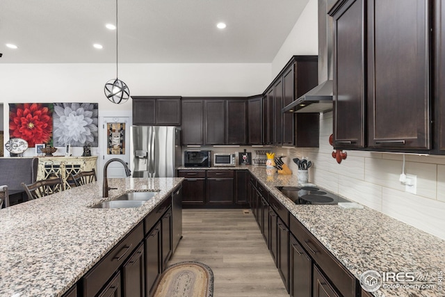 kitchen featuring wall chimney exhaust hood, sink, light stone counters, tasteful backsplash, and appliances with stainless steel finishes