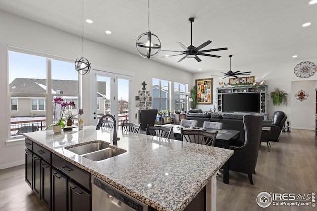 kitchen with sink, hanging light fixtures, light stone countertops, an island with sink, and stainless steel dishwasher