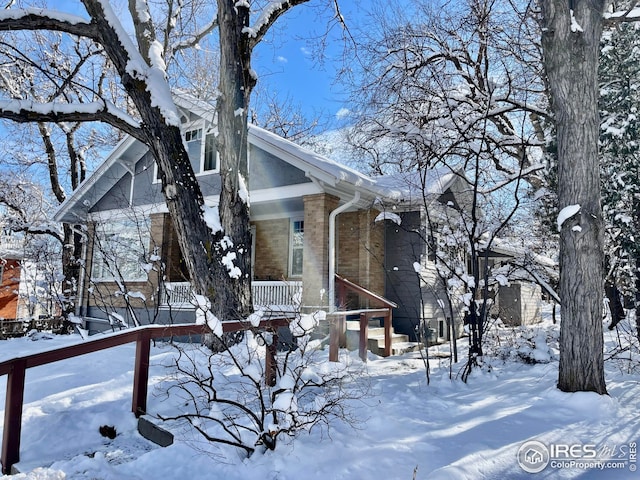 view of snowy exterior with a garage, covered porch, and brick siding