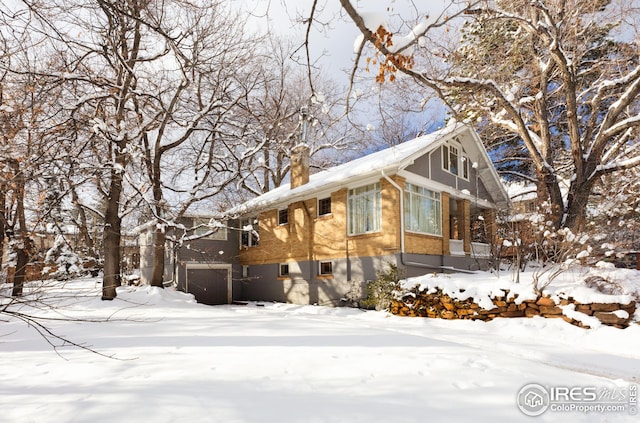 view of snowy exterior featuring an attached garage and a chimney