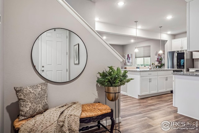 kitchen featuring light hardwood / wood-style floors, white cabinetry, light stone countertops, and stainless steel refrigerator